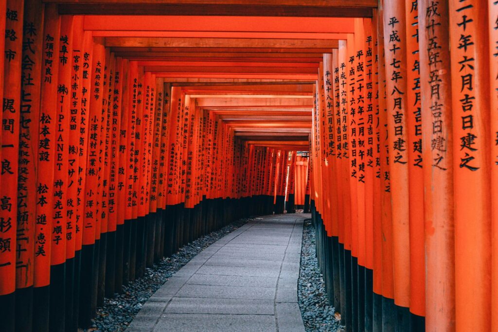 Dolga vrsta oranžnih Torii vrat v svetišču Fushimi Inari na Japonskem, simbol duhovnosti, tradicije in kulturne dediščine.