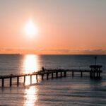 Burgas: Obmorski biser Bolgarije ob Črnem morju Slika pomola ob sončnem zahodu prikazuje mirno obmorsko vzdušje, kjer se nebo preliva v tople barve, morje pa odseva zlato svetlobo, kar ustvarja romantično in sproščujočo kuliso.