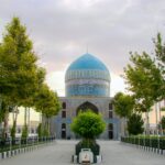 Turkmenistan: Čudovita dežela puščav, zgodovine in osupljive arhitekture Modra kupola mošeje v Ašgabatu, prestolnici Turkmenistana, obdana z zelenimi drevesi in mirnim mestnim okoljem.